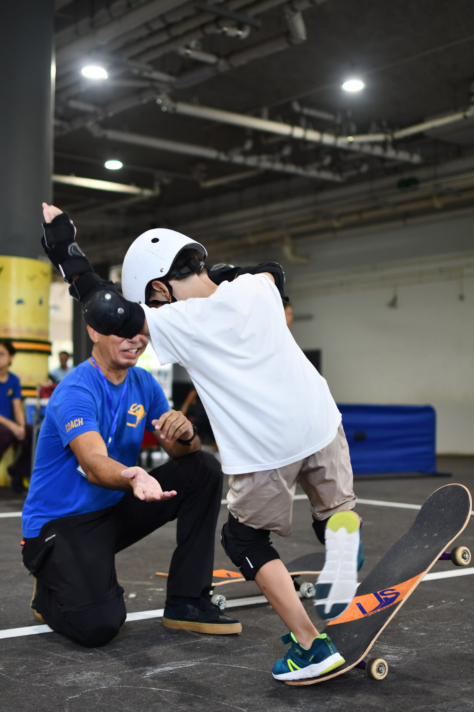 A skateboarding coach in protective gear supporting a participant on a board at a LyfeGo multi-sport event