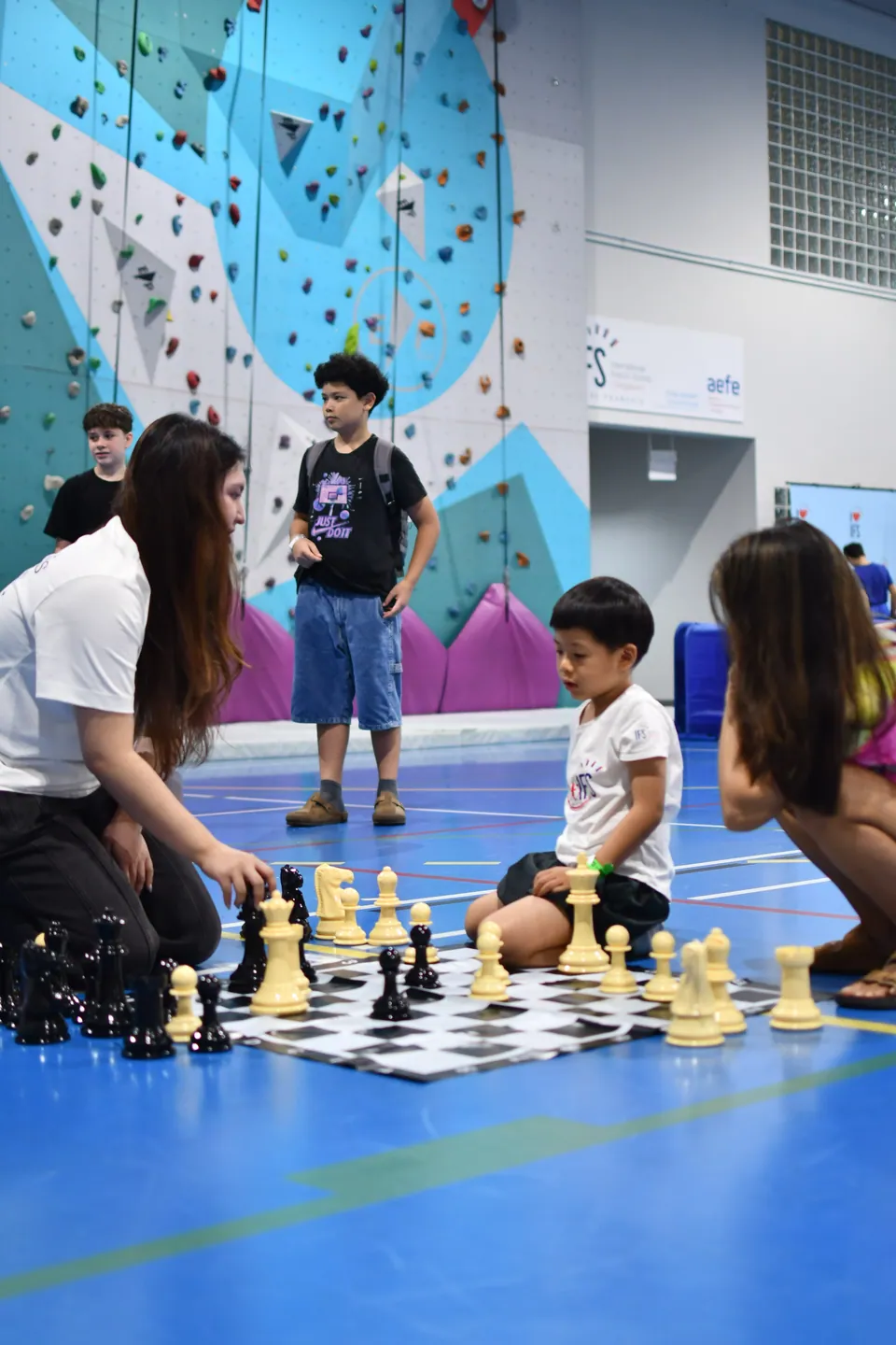 Young participants gathered around a giant chessboard in an indoor sports hall