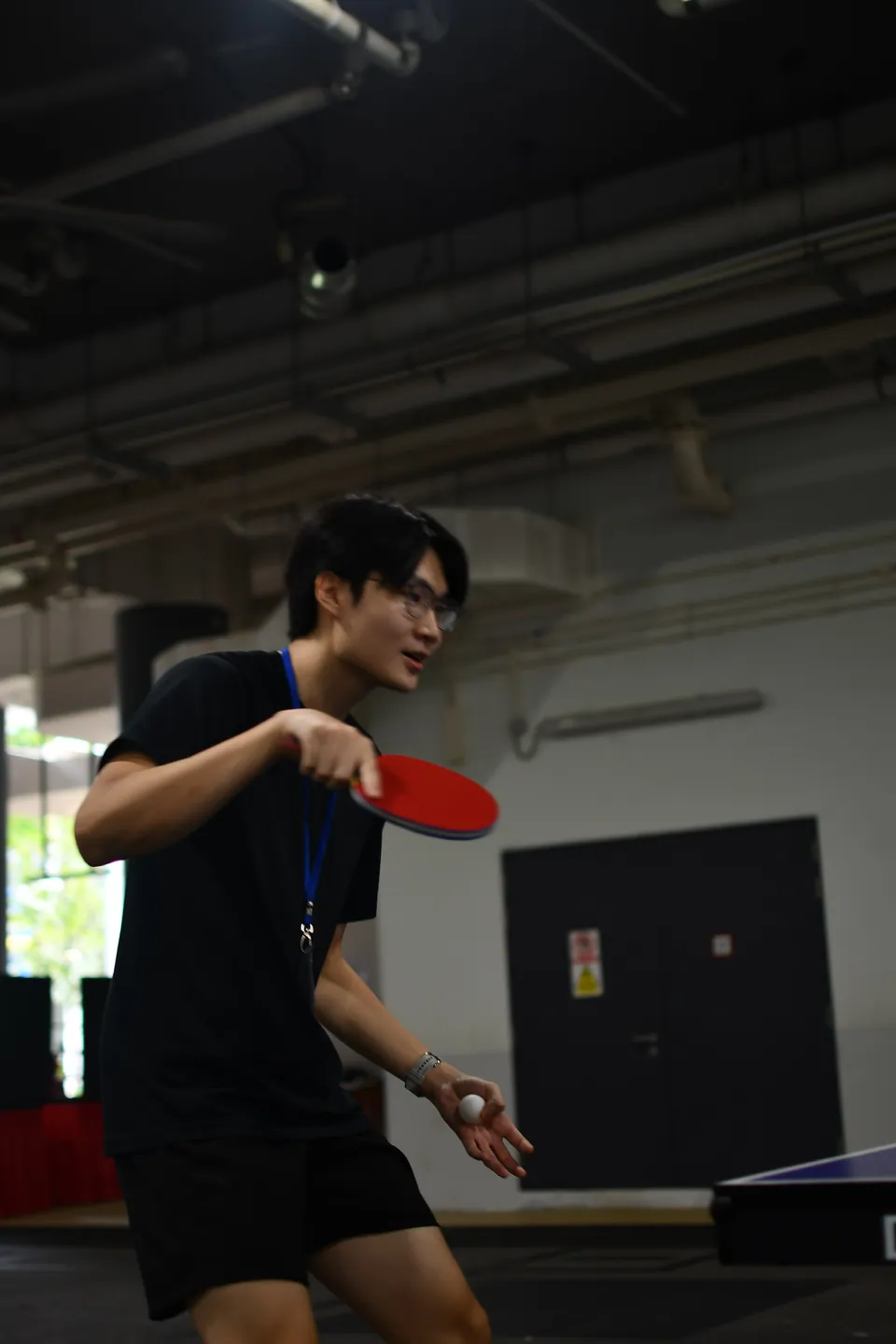 Participant holding a table-tennis paddle and ball beside an indoor table